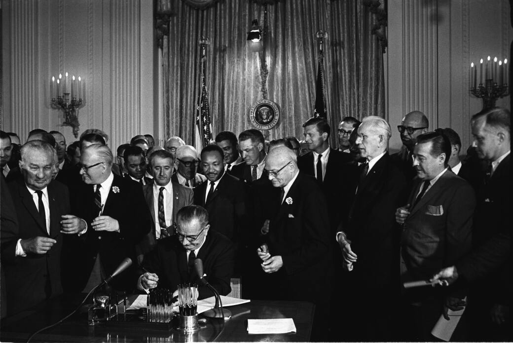 SIGNING THE CIVIL RIGHTS ACT, 1964: President Lyndon B. Johnson signs the act as Martin Luther King, Jr., and others, look on.