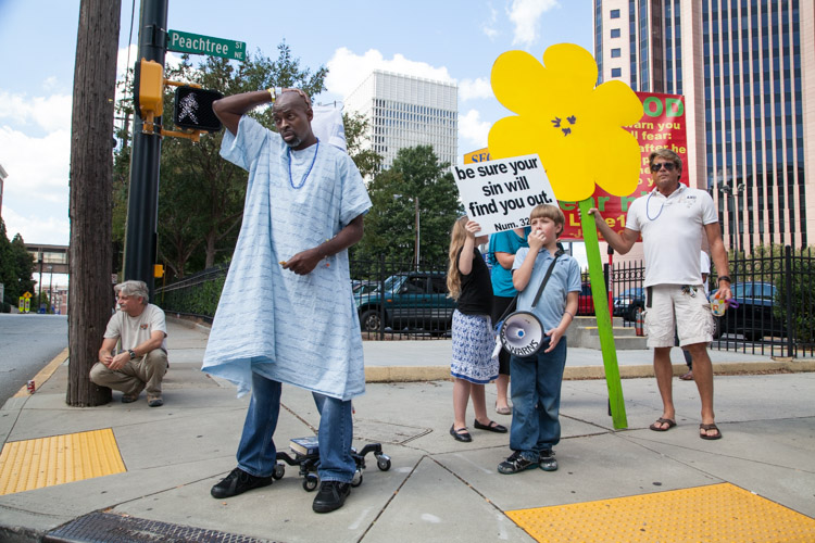 A patient from a nearby hospital watches the parade near a group of children protesting the parade.